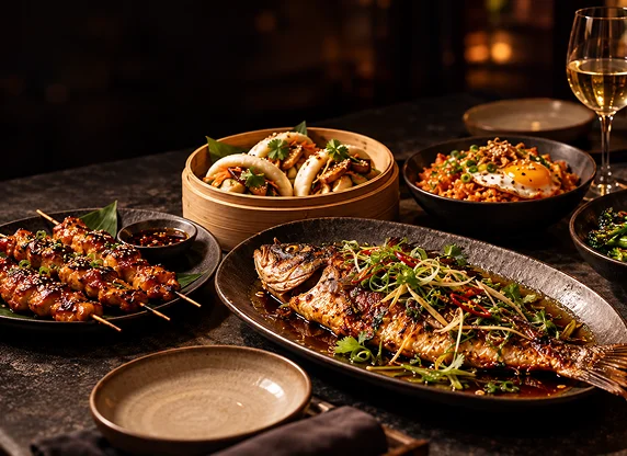 Grilled fish, chicken skewers, bao buns and side dishes on a restaurant table